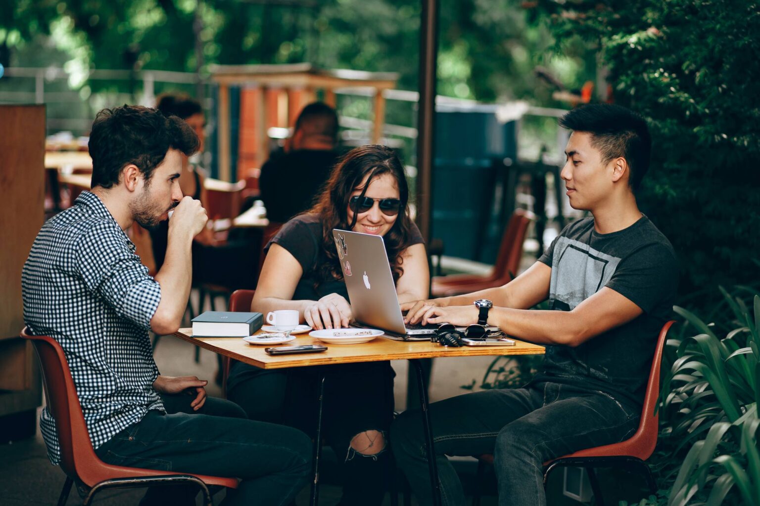 Three people around an outdoor cafe table, working together over a laptop