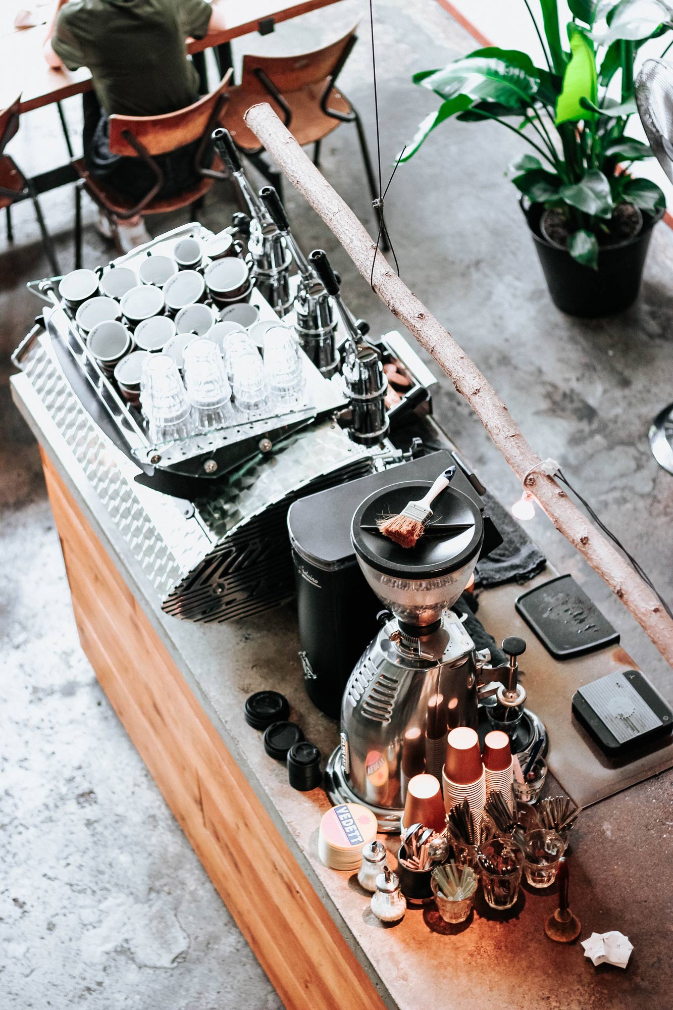 An espresso machine and grinder on a cafe counter, stacked with cups