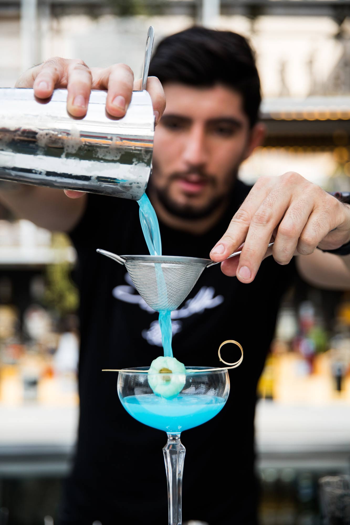 A bartender straining a cocktail into a glass